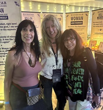 Heather Reilly Hiemstra stands between two guests for a group photo at the Rockstar Blends booth, the Rockstar Woman and Roll-On banners behind them at the Cannadelic Night Market.